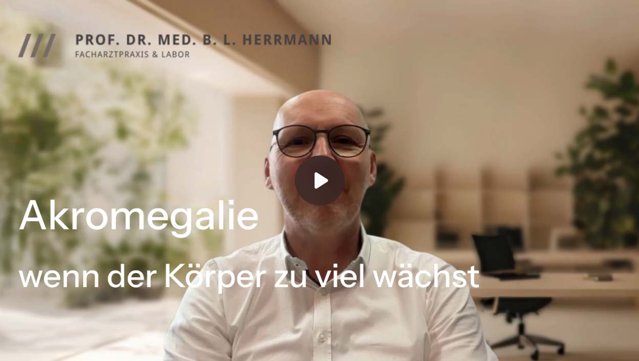 Prof. Dr. Herrmann und weißem Hemd vor einem Bildschirm mit Text und Play-Button